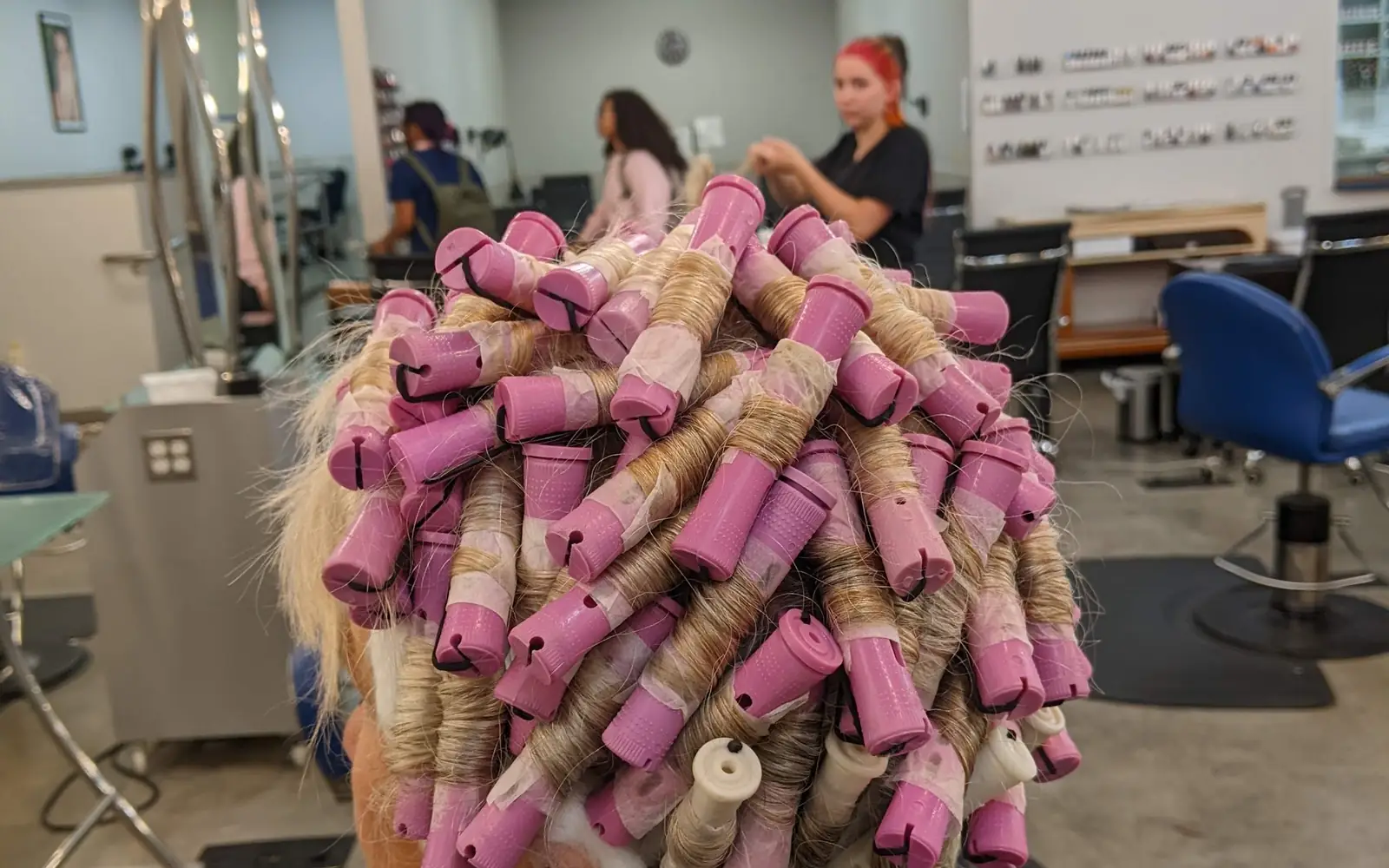 A client in pink perm rods on the Entourage clinic floor, with students working at the stations behind