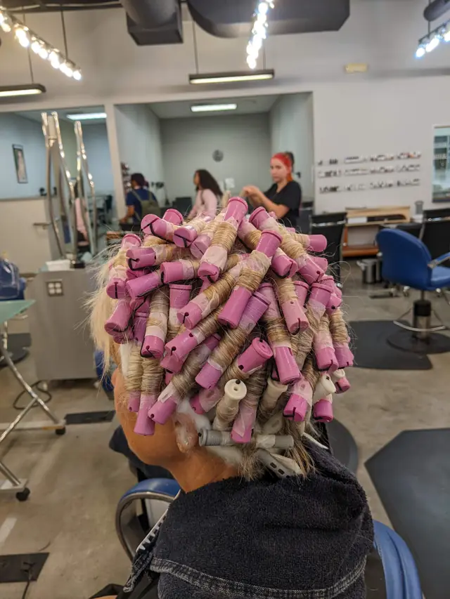 Students working at stations on the Entourage clinic floor behind a client in perm rods
